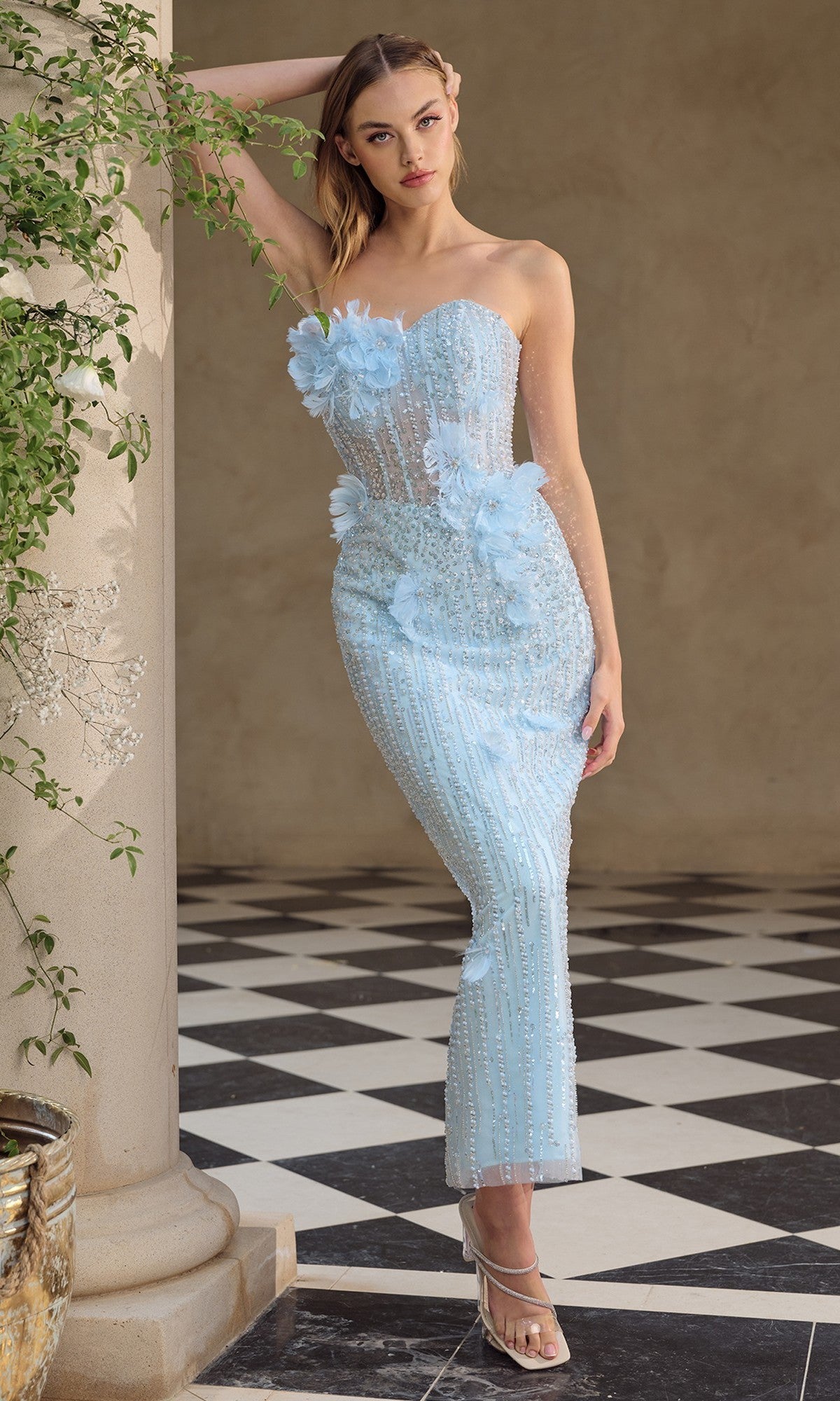 A woman in the Andrea & Leo A1487 tea-length formal dress in light blue stands against a column on a black-and-white checkered floor.